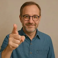 A middle-aged man with glasses, a salt-and-pepper beard, and a denim shirt smiles warmly while pointing at the camera, captured in a square-format image.